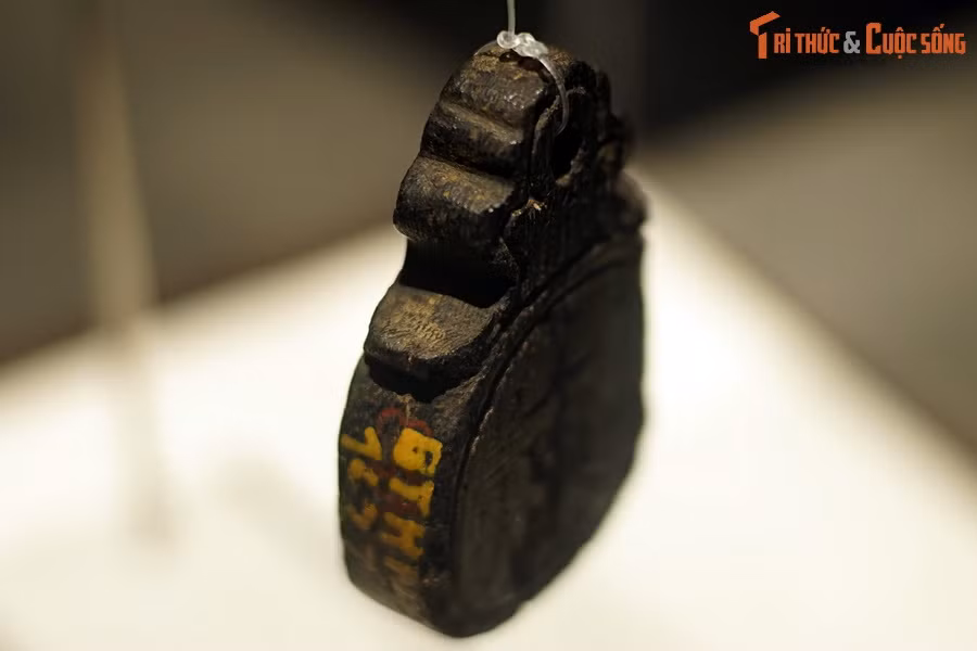 Một đầu thẻ bài có đục lỗ, dùng để buộc dây đeo, hai mặt khắc chìm một gờ rãnh tròn uốn lượn mềm mại theo dáng thẻ.