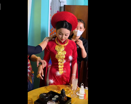 Đứng cạnh bên là cô dâu cũng đeo hàng chục chiếc kiềng vàng trên cổ, trong đó có nhiều chiếc kiềng vàng được thiết kế tinh xảo.