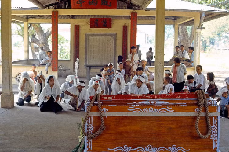 Một đám tang ở Sài Gòn. Gia quyến của người đã khuất đeo khăn tang trắng ngồi trước quan tài.