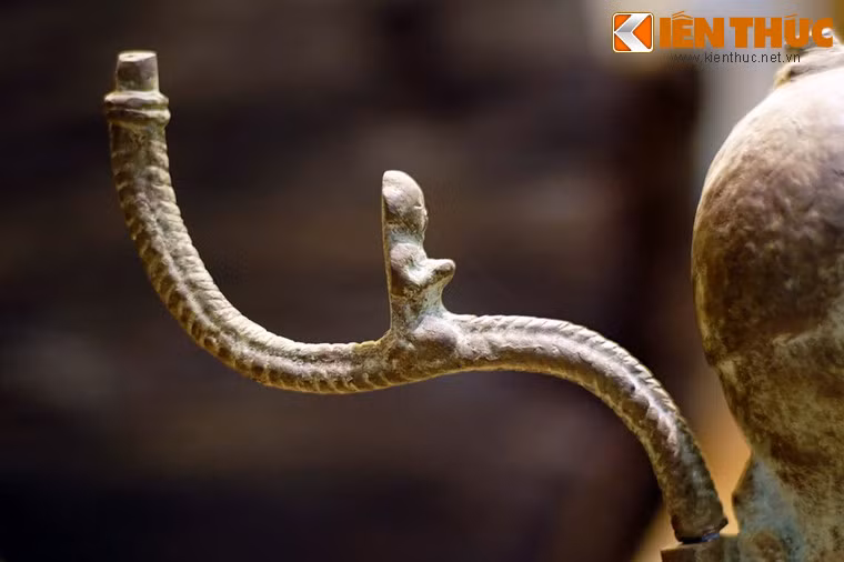 Hai vai và sau tượng gắn 3 cành chữ S, mỗi chữ S đỡ một đĩa đèn và gắn một hình người đang quỳ, được cho là các vũ công.