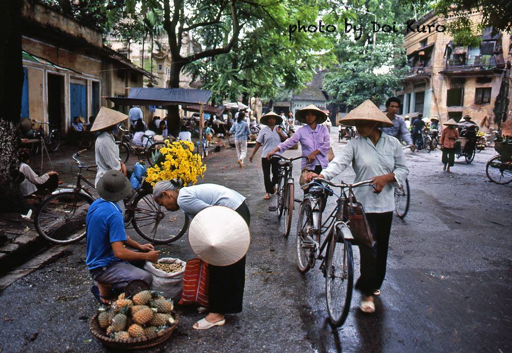 Những người phụ nữ dắt xe đạp đi chợ.