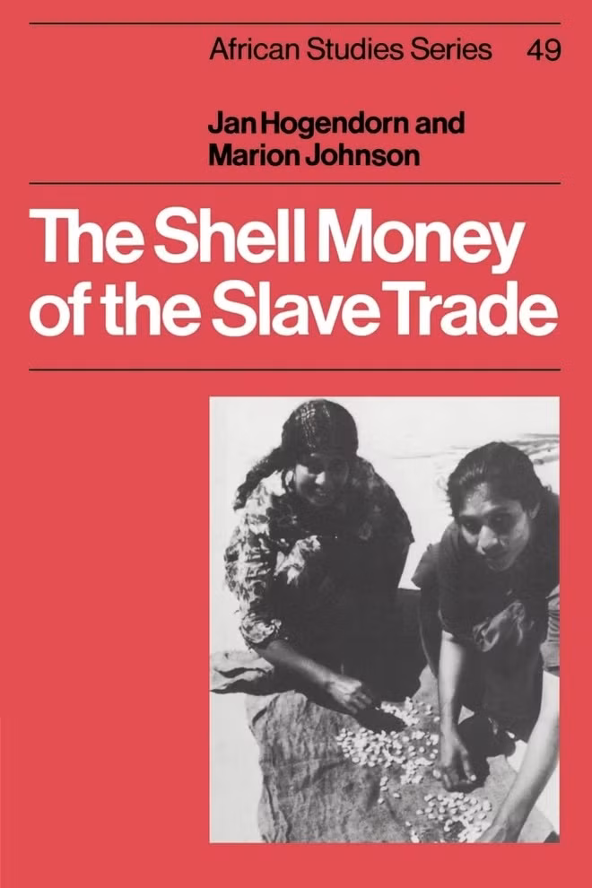 Shell money of the slave trade của Jan Hogendoorn và Marion Johnson. Vỏ sò Cowrie, ngôi nhà màu trắng bóng bẩy của một loài nhuyễn thể, chính là sự khẳng định đầu tiên của thế giới giàu có. Loại vỏ sò này được thu hoạch ở Maldives, bán ở Bengal, vận chuyển đến châu Âu (chủ yếu là Hà Lan và Anh) và được dùng để mua nô lệ ở Tây Phi. Vỏ sò này cũng đã đi xuyên Đại Tây Dương: một chiếc vỏ sò được tìm thấy tại điền trang của Thomas Jefferson trong khi một số lượng lớn được phát hiện gần các chợ nô lệ ở Virginia và một số vẫn được người Brazil gốc Phi sử dụng cho đến ngày nay để xem bói. Vai trò ghê gớm đó khiến Cowrie trở thành một trong những loại tiền quan trọng nhất còn được tìm thấy trong lịch sử. Jan Hogendoorn và Marion Johnson đã theo dõi câu chuyện này từ những lời kể đầu tiên của các du khách Ả Rập cho đến sự biến mất vào cuối những năm 1960 - thời điểm nó chỉ tồn tại ở những vùng hẻo lánh ở nông thôn Tây Phi. Ảnh: Amazon.