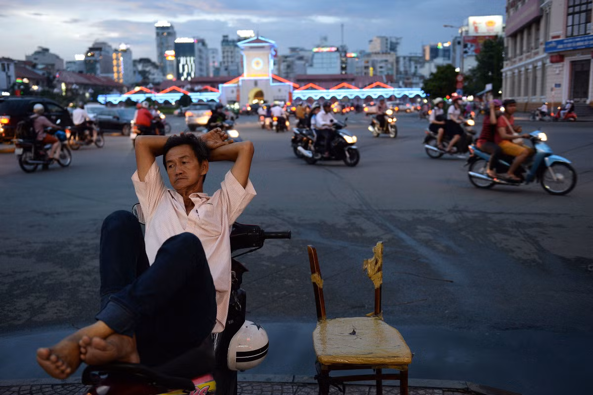 Người đàn ông làm nghề xe ôm ngả lưng trên xe tại một ngã tư đông đúc vào lúc chiều tối. Ảnh USN