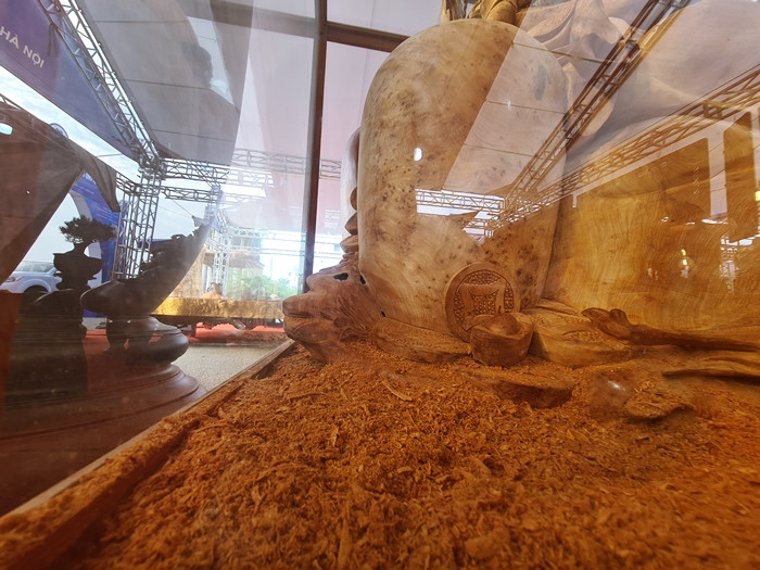 Dưới chân tác phẩm “Di Lặc tựa chum ngũ tặc” là những mùn gỗ mà theo anh Long đây là tượng trưng cho những “bông tuyết”.