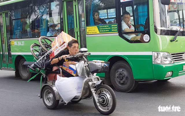 Hình ảnh người đàn ông tàn tật này khom người, một tay cầm lái, một tay còn lại ôm chặt thùng mì gói chạy xe trên đường để mang quà Tết đến với những người đồng cảnh ngộ khiến không ít người đi đường phải ngoái nhìn - Ảnh: NGỌC HIỂN