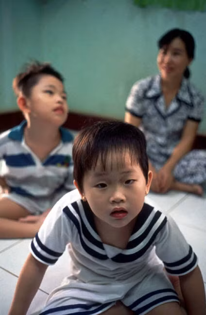 Bé gái Đỗ Thùy Vân bên em trai và mẹ. Cả hai em bị bại não do di chứng chất độc da cam. Ảnh: Chris Steele-Perkins/ Magnum Photos.