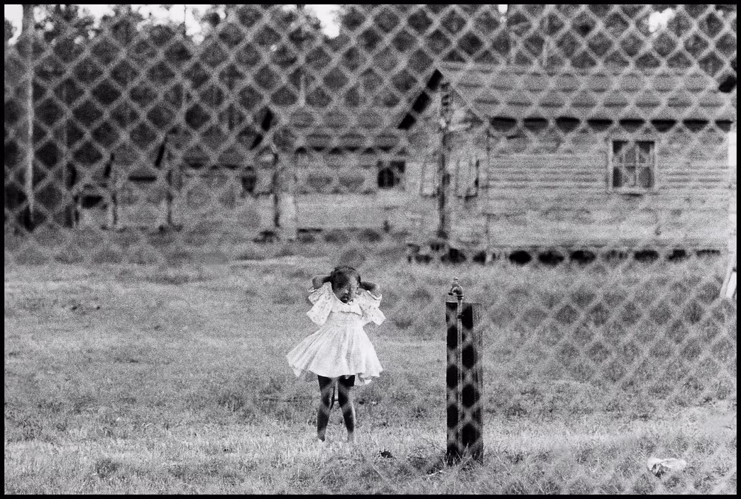 Bé gái da đen đứng sau hàng rào mắt cáo của trại tạm cư ở Nam Carolina, 1962. Ảnh: Bruce Davidson/ Magnum Photos.