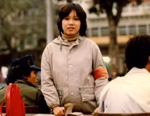 Thiếu nữ "băng đỏ" xinh đẹp với một trong những cách mặc thời trang nhất giữa thập niên 80: Áo len cổ lọ bên trong, áo lông Đức bên ngoài. Người ngồi bên cạnh cũng rất hợp thời cùng áo Nato và mũ bò kiểu Levi's. Ảnh: Khampha.vn.