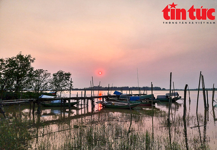 Vào thời khắc chuyển giao cuối ngày, mặt trời đỏ rực như quả cầu lửa, nhuộm hồng bầu trời và in bóng xuống lòng sông.