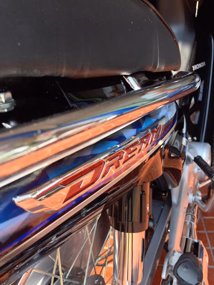 Dòng chữ Dream ở hai bên thân xe cũng được đúc bằng nhựa, sau đó mạ chrome và tiếp tục sơn đỏ ở phía trong. Những chi tiết cầu kỳ này đã khiến Dream 125 trở nên cao cấp hơn hẳn các thế hệ trước.