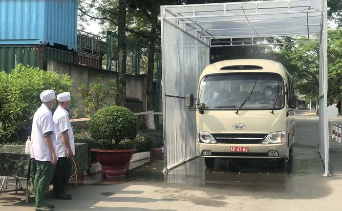 Cụ thể, đoàn xe chở công dân từ sân bay về sẽ được sát khuẩn tại cổng sư đoàn, sau đó người dân xuống xe và thực hiện tuần tự các bước gồm nhận kính và khử khuẩn tay, đi qua buồng khử khuẩn. Tiếp đó là bàn bỏ kính, sau đó tới bàn cấp khẩu trang và khử khuẩn tay, kế tiếp qua bàn kiểm tra thân nhiệt và nhận tờ khai y tế. Sau đó là khu vực kê khai y tế. Khoảng 9 giờ, xe chở các công dân từ vùng dịch về đến Sư đoàn 317. Tại đây chiếc xe phải đi qua cổng sát khuẩn. Ảnh: MINH TÂM