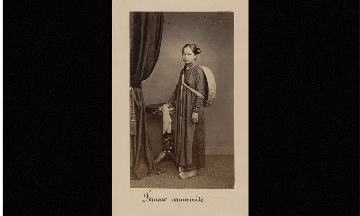 Ảnh một người phụ nữ mặc áo dài, tóc búi kiểu bánh lái, khoác phía sau lưng chiếc nón cụ. (Nguồn: Émile Gsell)