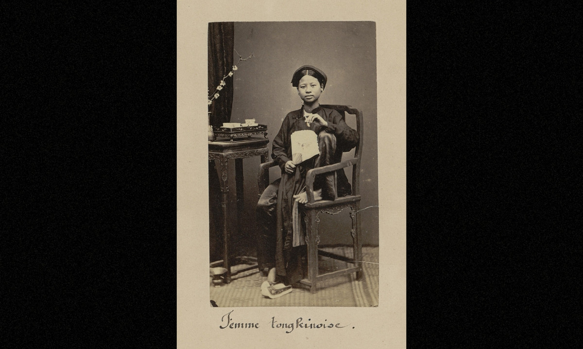 Ảnh thiếu nữ xứ Bắc Kỳ cầm quạt, đầu đội khăn xếp, ngồi trên ghế gỗ. (Nguồn: Émile Gsell)