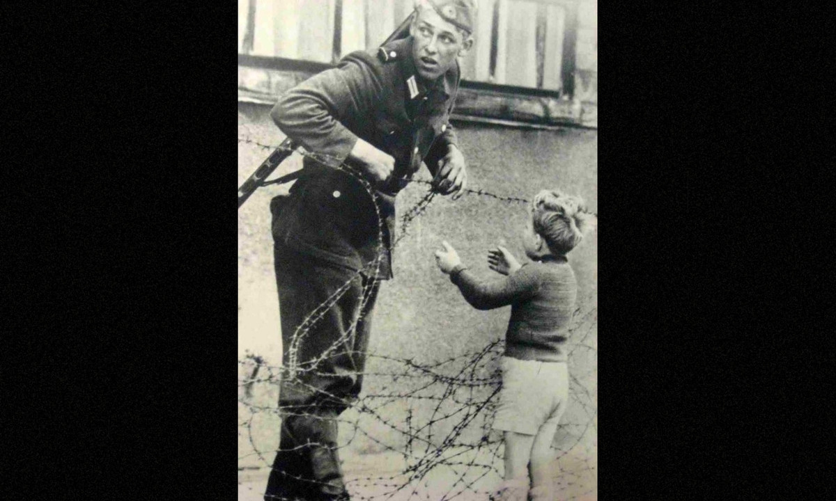 Một người lính đang giúp một cậu bé vượt qua Bức tường Berlin. Đây là một trong những bức ảnh lịch sử ghi dấu thời khắc vô cùng quan trọng. (Nguồn: Brightside)