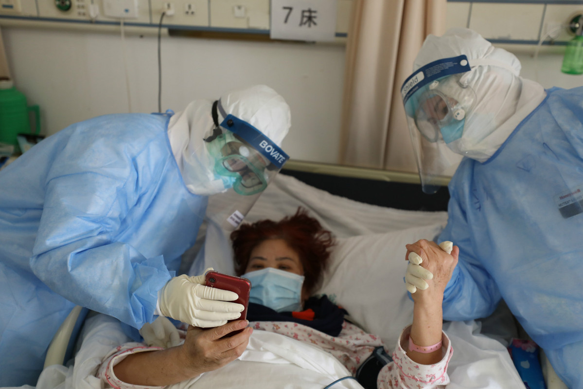 Hai y tá giúp một bệnh nhân xem điện thoại di động trong phòng cách ly tại Bệnh viện Chữ Thập đỏ Vũ Hán ngày 16/2. Ảnh: CD.