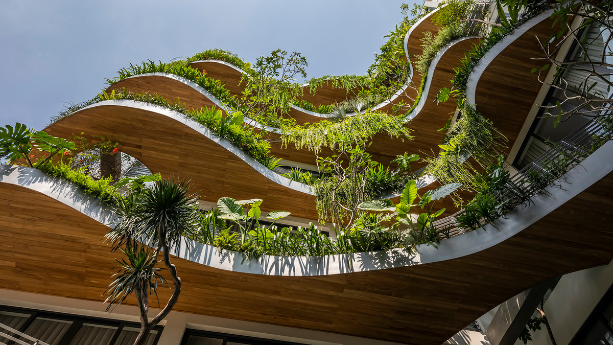 Mặt tiền của ngôi nhà được tạo nên từ những đường cong tự nhiên và được bao bọc bởi lớp cây xanh với nhiều loại cây nhiệt đới nhỏ.