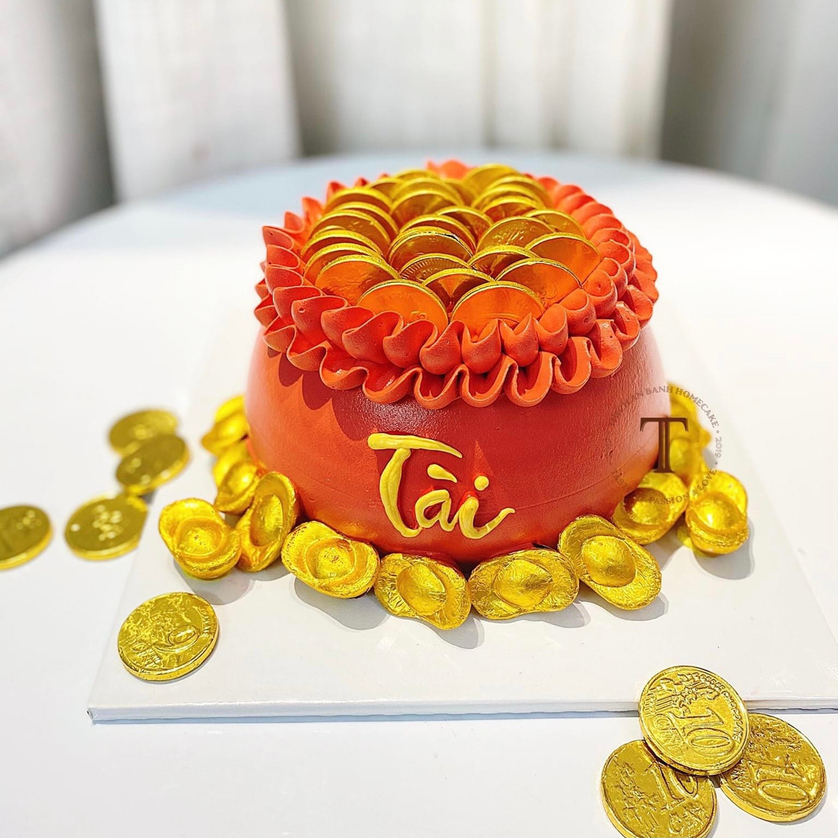 Bánh được trang trí bắt mắt với nơ đỏ, lớp phủ giả vàng ăn được cùng điểm nhấn là những thỏi chocolate hình đồng vàng, thỏi vàng tượng trưng cho tài lộc dồi dào. Ảnh: Facebook