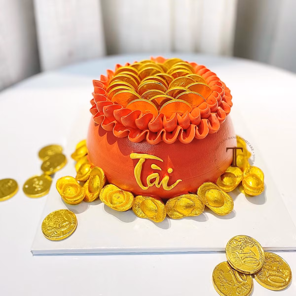 Bánh được trang trí bắt mắt với nơ đỏ, lớp phủ giả vàng ăn được cùng điểm nhấn là những thỏi chocolate hình đồng vàng, thỏi vàng tượng trưng cho tài lộc dồi dào. Ảnh: Facebook