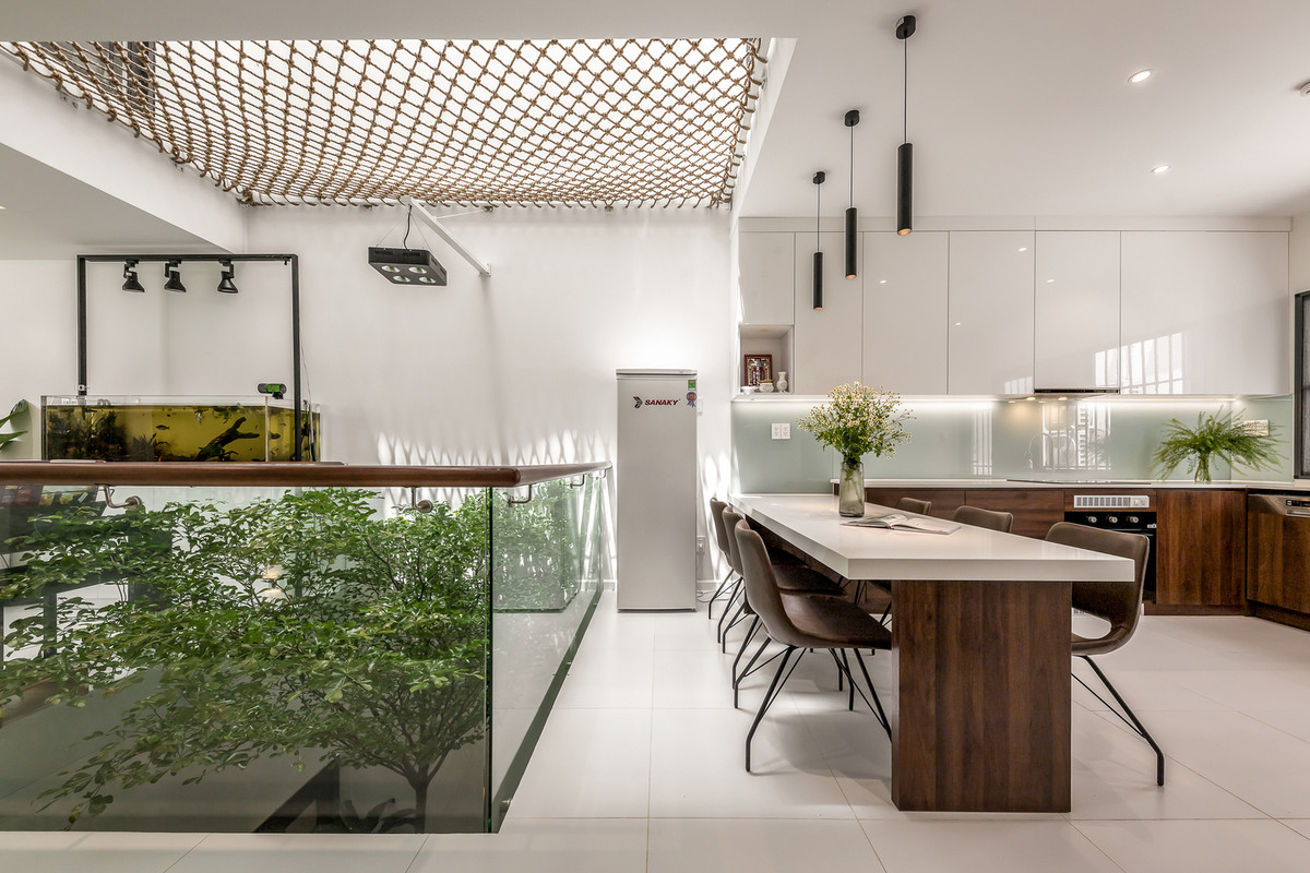 Bếp và nhà ăn rộng rãi, bao quanh là tán cây xum xuê được ngăn cách qua lớp kính bo góc theo hành lang của căn phòng.