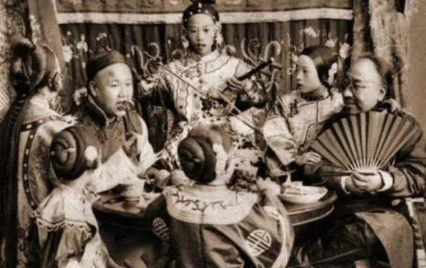 Hai thương nhân giàu có dùng bữa. Bên cạnh họ là những người phụ nữ đàn hát, trò chuyện với khách.