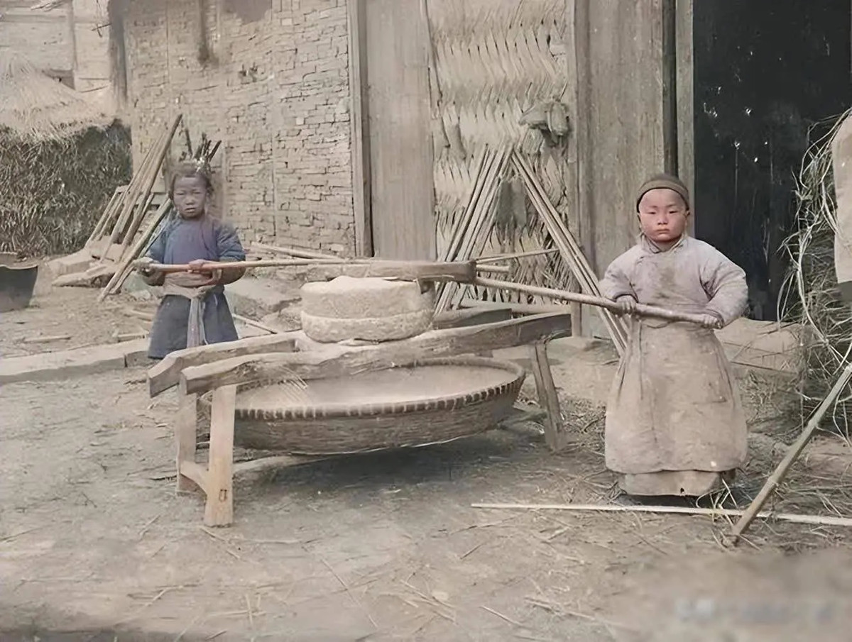 Hai em bé kéo cối xay trước nhà.