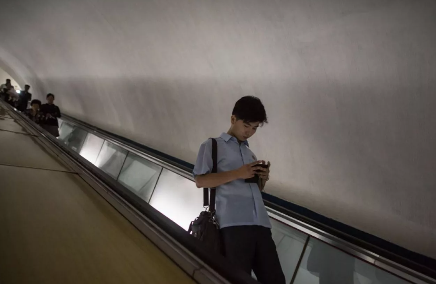 Người đàn ông xem điện thoại khi đi xuống thang cuốn trong một ga tàu điện ngầm ở Bình Nhưỡng.
