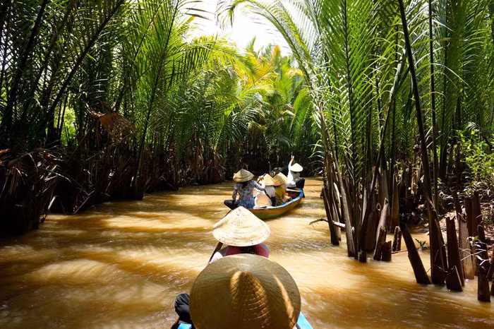 Các phụ nữ trong trang phục áo bà ba, đội nón lá truyền thống đang chèo xuồng hướng dẫn du khách trải nghiệm khám phá miền sông nước Cửu Long - Ảnh: Getty