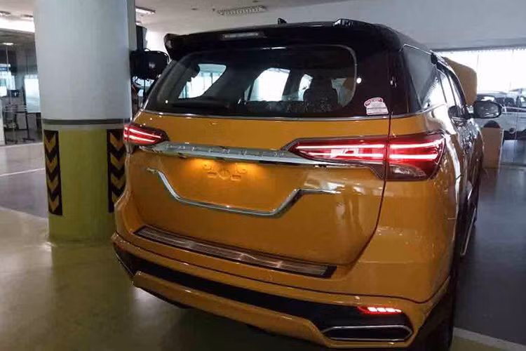 Chưa hết, chiếc xe Toyota Fortuner đời mới này còn được lắp cản va trước hầm hố tích hợp bộ chẻ khí mới, dải đèn LED định vị ban ngày và những chi tiết trang trí màu bạc. Đằng sau xe xuất hiện cản va sau mới và 2 ống xả giả. Tiếp đến là màu sơn cam rực rỡ, nóc xe màu đen bóng và viền màu đen xung quanh đèn pha cũng như đèn hậu.