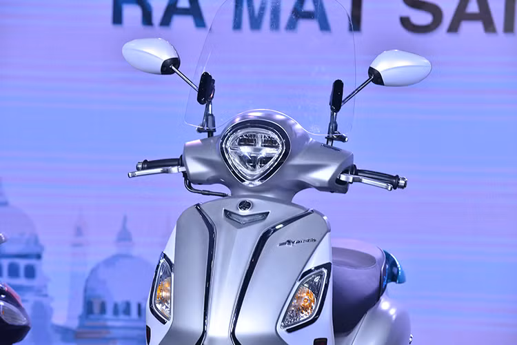 Đáng chú ý là phần đầu Yamaha Grande Hybrid 2018 đã thon gọn hơn so với đời cũ. Chưa hết, đèn pha trên mẫu xe ga mới này còn được Yamaha thiết kế 2 tầng cá tính và sử dụng bóng Full LED tăng khả năng chiếu sáng. Ngoài ra, cặp gương theo xe với 3 màu là crôm, bạc và đen.