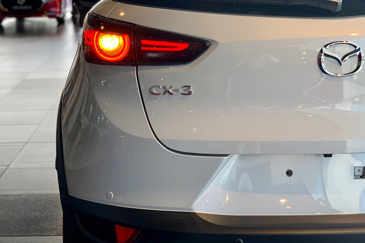 Cụ thể, Mazda CX-3 1.5L AT 2023 mới chỉ được trang bị đèn pha, đèn LED chạy ban ngày và đèn hậu dùng bóng Halogen thay vì LED. Bên cạnh đó, xe còn thiếu tính năng tự động bật/tắt đèn trước và tự động cân bằng góc chiếu. Vành la-zăng của bản tiêu chuẩn này vẫn có đường kính 18 inch trong khi gương chiếu hậu là loại gập điện/chỉnh điện.