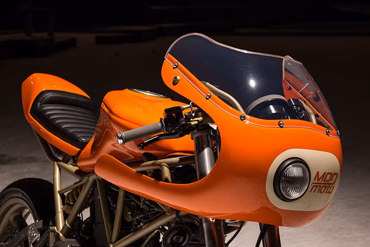 Phần đầu xe được Mod moto gò một ốp quây lớn bao gồm kính núp gió lớn cùng mặt nạ với đèn một mắt cực ngầu. Phần đầu được phối màu cam và trắng, sát đèn pha là logo thương hiệu Mod moto.