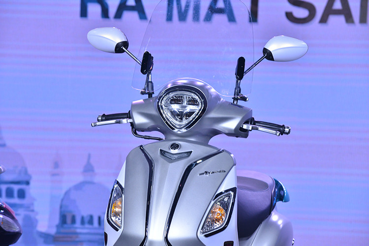Đáng chú ý là phần đầu Yamaha Grande Hybrid mới đã thon gọn hơn so với đời cũ. Chưa hết, đèn pha trên mẫu xe ga mới này còn được Yamaha thiết kế 2 tầng cá tính và sử dụng bóng Full LED tăng khả năng chiếu sáng. Ngoài ra, cặp gương theo xe với 3 màu là crôm, bạc và đen.