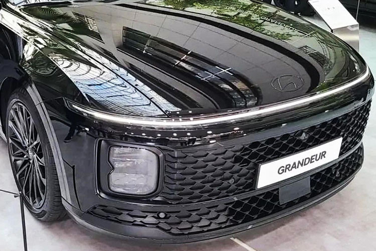 Trên đầu xe, mẫu sedan hạng trung này được trang bị lưới tản nhiệt và hốc gió trung tâm đều được thiết kế hình chữ nhật cỡ lớn với mắt lưới dạng mắt cáo. Nằm giữa 2 chi tiết này là nẹp khá mỏng, sơn cùng màu thân xe. Tiếp đến là cụm đèn pha nằm dọc mới và dải đèn LED định vị ban ngày vắt ngang đầu xe, tương tự cặp đôi xe đa dụng Hyundai Stargazer và Staria.