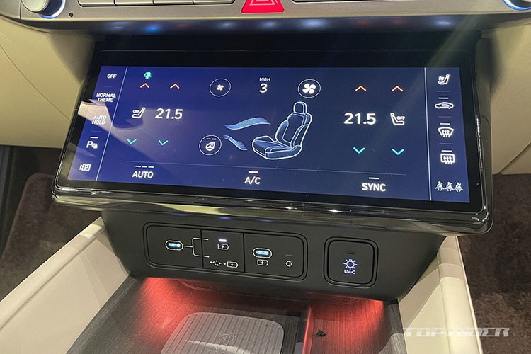 Bên dưới cửa gió là hàng nút bấm cơ học, màn hình cảm ứng 10,25 inch để chỉnh điều hòa, các cổng USB, sạc điện thoại không dây và ngăn chứa đồ có nắp che.