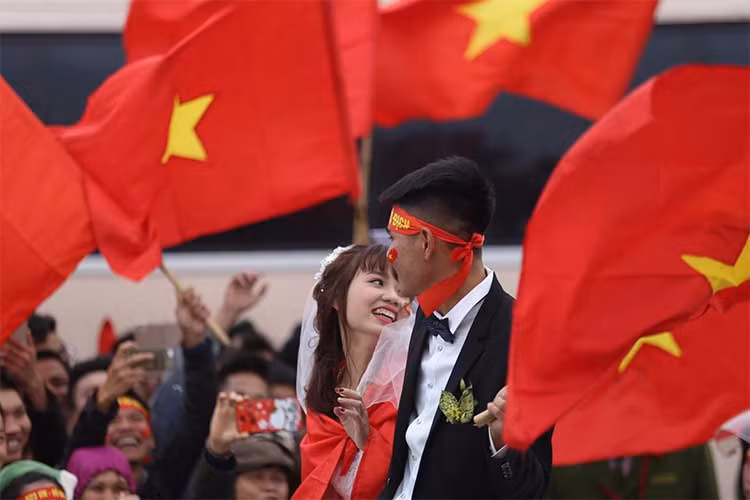 Trái ngược với lo lắng của mọi người, trong ảnh cô dâu và chú rể vẫn cười tươi, tay họ còn cầm theo lá quốc kỳ hòa vào dòng người đang đi đón đội tuyển U23 Việt Nam trở về và thậm chí còn hô "Việt Nam vô địch".
