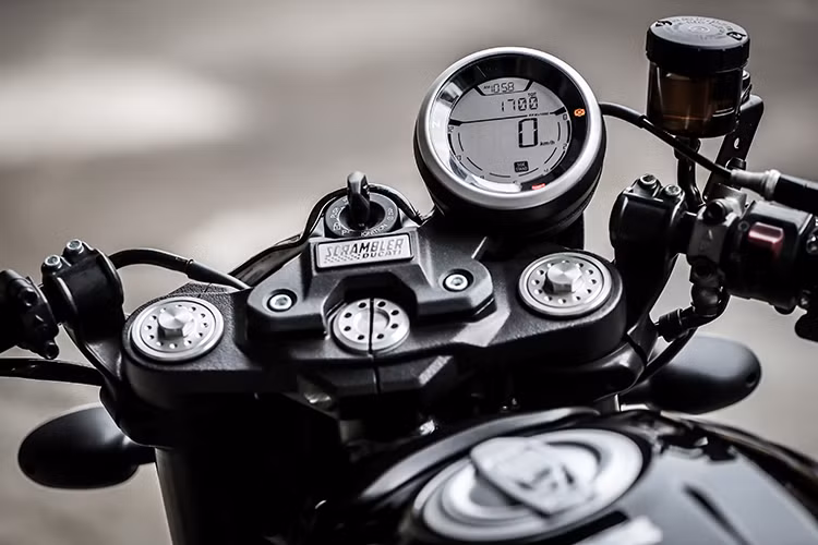Theo đúng phong cách cafe racer, Scrambler Cafe Racer được trang bị cặp tay lái clip-on thể thao, với 2 đầu tay lái là cặp gương hậu gắn gù gọn gàng. Để che đi lỗ bắt gù ghi-đông trên chảng ba, Ducati đã sử dụng một tấm thép với bảng tên Scrambler khá đẹp mắt. Đồng hồ điện tử tròn của xe hoàn toàn không có thay đổi so với các bản Scrambler trước.