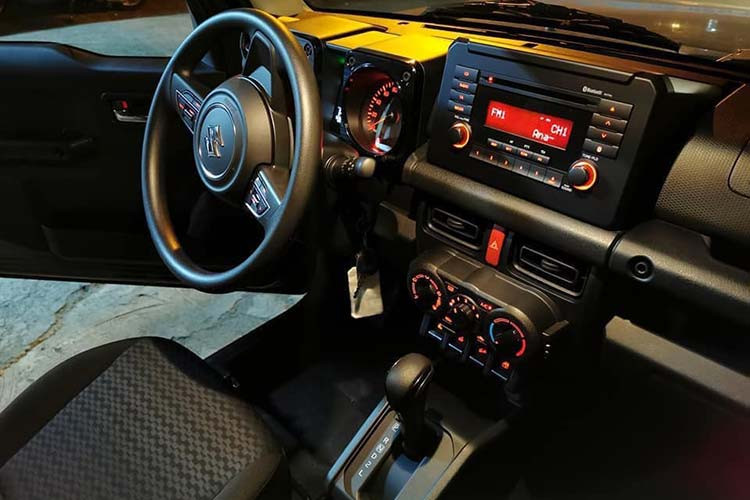 Bên trong Suzuki Jimny 2019 mới, khách hàng sẽ tìm thấy những trang bị như vô lăng 3 chấu bọc da, chỉnh điện 2 hướng, tích hợp phím chức năng, cửa sổ chỉnh điện bên ghế lái, khóa điều khiển từ xa, hệ thống điều hòa tự động với lọc không khí, màn hình đa thông tin trong bảng đồng hồ, tay nắm cửa mạ crôm, ghế bọc nỉ màu đen, ghế lái chỉnh tay 6 hướng...