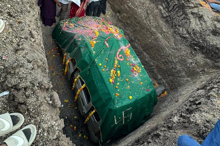 Chiếc ôtô cũ có vẻ là mẫu xe Suzuki Maruti Wagon R đời 2010 sản xuất tại Ấn Độ. Xe được trang trí bằng vòng hoa xung quanh thân, nóc đầy cánh hoa hồng. Sau khi chiếc xe yên vị trong hố, người ta đã phủ lên một tấm khăn màu xanh lá cây và mọi người rải cánh hoa lên đó.