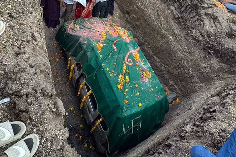 Chiếc ôtô cũ có vẻ là mẫu xe Suzuki Maruti Wagon R đời 2010 sản xuất tại Ấn Độ. Xe được trang trí bằng vòng hoa xung quanh thân, nóc đầy cánh hoa hồng. Sau khi chiếc xe yên vị trong hố, người ta đã phủ lên một tấm khăn màu xanh lá cây và mọi người rải cánh hoa lên đó.