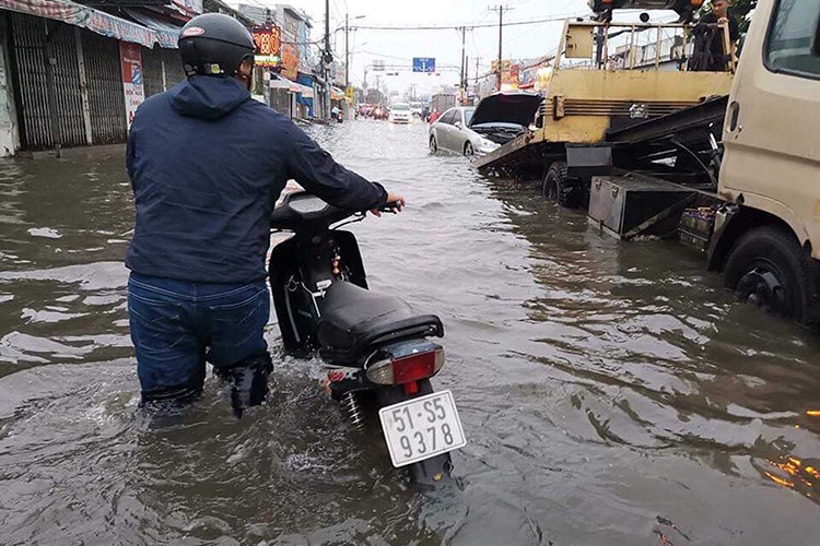 Trong ảnh là một chiếc xe máy Honda Wave chết máy do ngập nước được chủ nhân dắt bộ về nhà, phía trước là một chiếc xe sang Mercedes-Benz phiên bản S bị chết máy và đang được đưa lên xe cứu hộ.