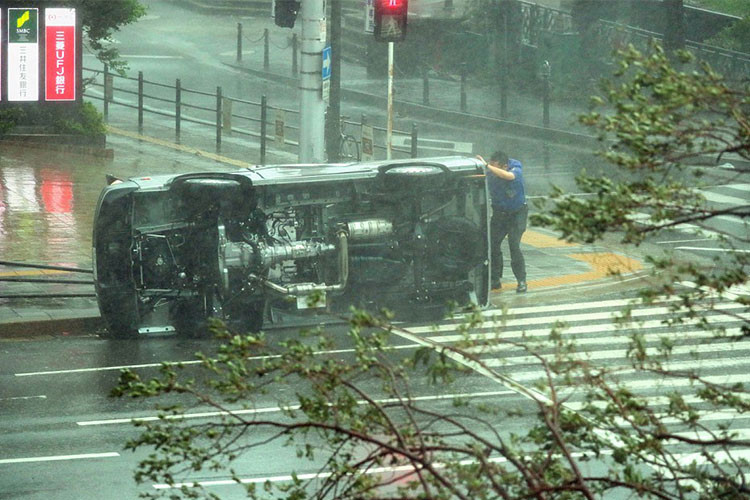 Một chiếc xe bị lốc cuốn nằm phơi bụng cùng với chủ nhân núp sau.