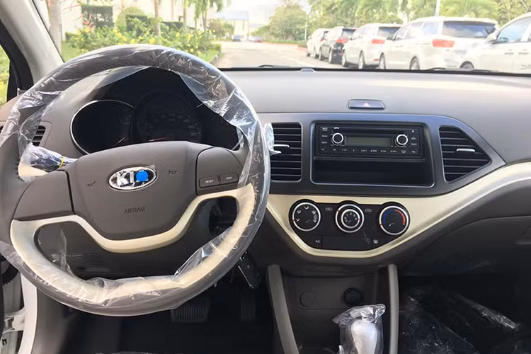 Bên trong xe, khu vực cần số là khác biệt lớn nhất với Morning EX MT. Vô lăng 2 chấu đơn giản với 2 nút bấm điều chỉnh thông số trên đồng hồ. Kia Morning AT mới cũng giống bản giá rẻ, không có màn hình trung tâm, chỉ có radio và các núm chỉnh điều hòa.