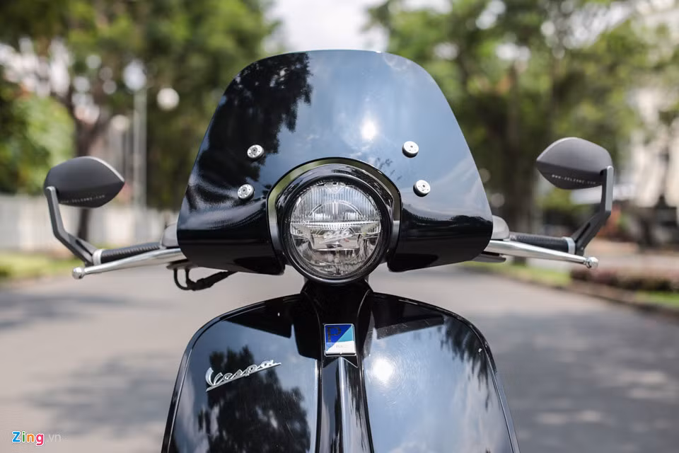 Phía trước là phần kính chắn gió dành riêng cho Vespa 946. Phần kính chắn này không đi kèm theo xe nguyên bản, chủ xe phải bỏ ra số tiền hơn 10 triệu đồng để thêm vào. Hai bên tay lái là cặp kính gù của Zelioni mang lại vẻ ngoài hiện đại, thể thao hơn.