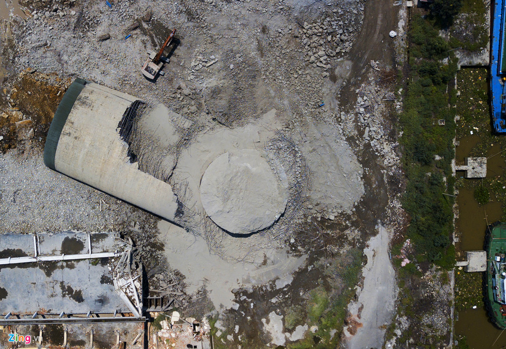 3 máy cuốc, đục phá từng mảng bê tông, các công nhân cắt dọn những thanh thép các loại thành từng đống trước khi đưa lên xe chuyển đi. Một trong các bể chứa nhỏ hơn đã được cho đổ hoàn toàn trước đó. Bên bờ sông, các tàu chở container, tàu kéo vẫn neo đậu chờ ra vào cảng.