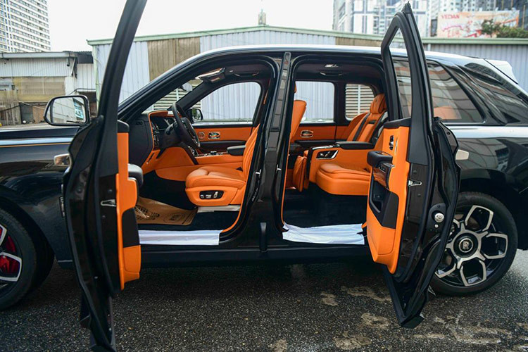Mở cửa bước vào bên trong khoang lái, chiếc xe SUV siêu sang Rolls-Royce Cullinan Black Badge 2024 đang được chào bán có nội thất bọc da màu cam Hermes và điểm ấn tượng là rất nhiều chi tiết của khoang lái ốp carbon bóng đắt tiền.