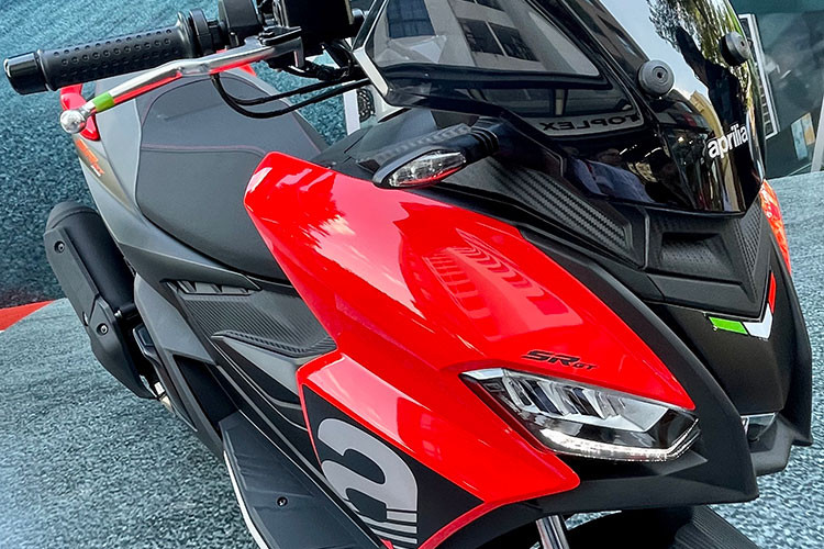 Cụm đèn chiếu sáng trước của mẫu xe tay ga thể thao nhà Aprilia được chia thành 3 ngăn riêng biệt, 2 bên là đèn chiếu gần và ở giữa là đèn chiếu xa. Phía trên được lắp kính chắn gió màu khói tương đối cao và rộng.