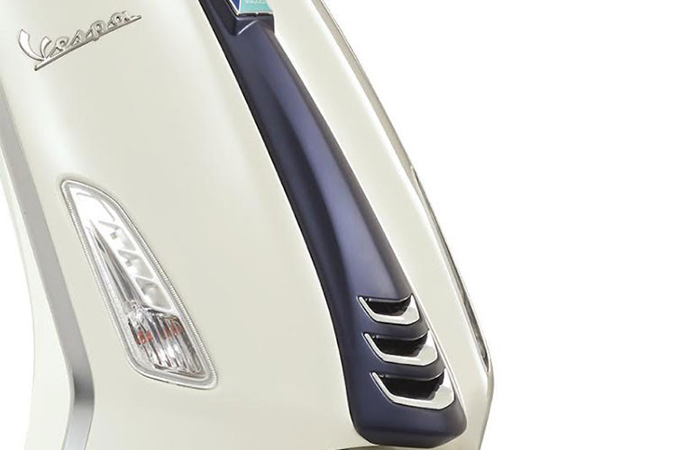 Những nét chấm phá tinh tế nổi bật trên nền trắng của bức tranh Vespa là logo “Yacht Club” dập nổi trên cốp đựng đồ phía trước, cà vạt màu xanh nhám mạ crome, đường sọc xanh đặc trưng chạy dọc thân xe.