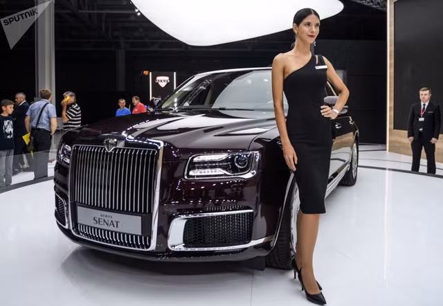 Một cô nàng người mẫu đang tạo dáng bên mẫu xe sang Aurus Senat 2019 phiên bản "dân sự" của mẫu limousine phục vụ Tổng thống Nga Vladimir Putin. Mẫu xe này có vẻ ngoài khá giống xe Rolls-Royce.