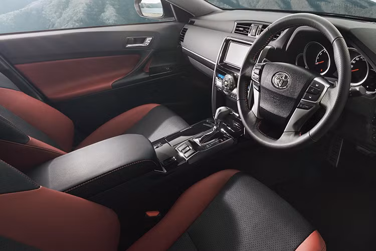 Bên trong Toyota Mark X Final Edition 2019 xuất hiện không gian nội thất phối 2 màu đen - đỏ tương phản, đậm chất thể thao. Ghế và mặt cửa của phiên bản đặc biệt này đều được bọc bằng chất liệu da tổng hợp. Trong khi đó, trên vô lăng 4 chấu, cần số, mặt cửa, ghế và bệ tì tay đều có chỉ khâu màu đỏ làm điểm nhấn.