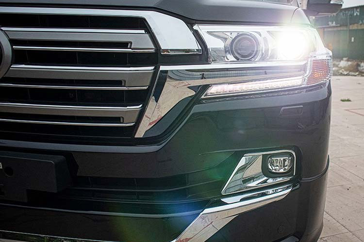 Phần đầu xe, Toyota Land Cruiser 5.7L 2020 nhập khẩu vẫn thể hiện sự hầm hố với cụm lưới tản nhiệt 3 thanh ngang to bản và viền mạ crom nối liền với cụm đèn trước Full-Led. Đèn pha của mẫu SUV 8 chỗ này là bóng LED Projector kèm đèn chạy ban ngày dạng LED, trong khi đó đèn sương mù tách biệt ở phần cản dưới cũng có chi tiết mạ crom.